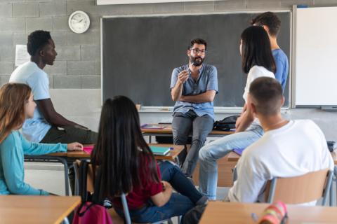 Teacher talking with young students seating in a circle at school 