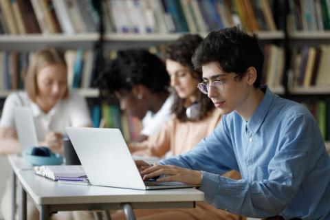 university students sitting in library, reading and on laptops