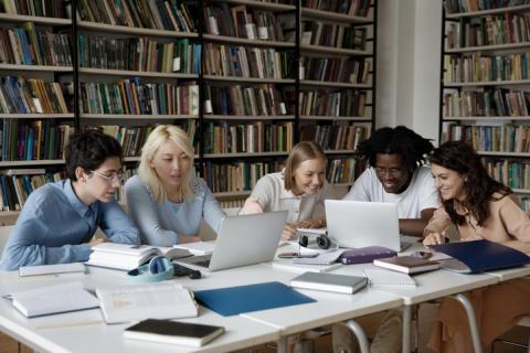 Group of multiethnic students studying together in library using laptop